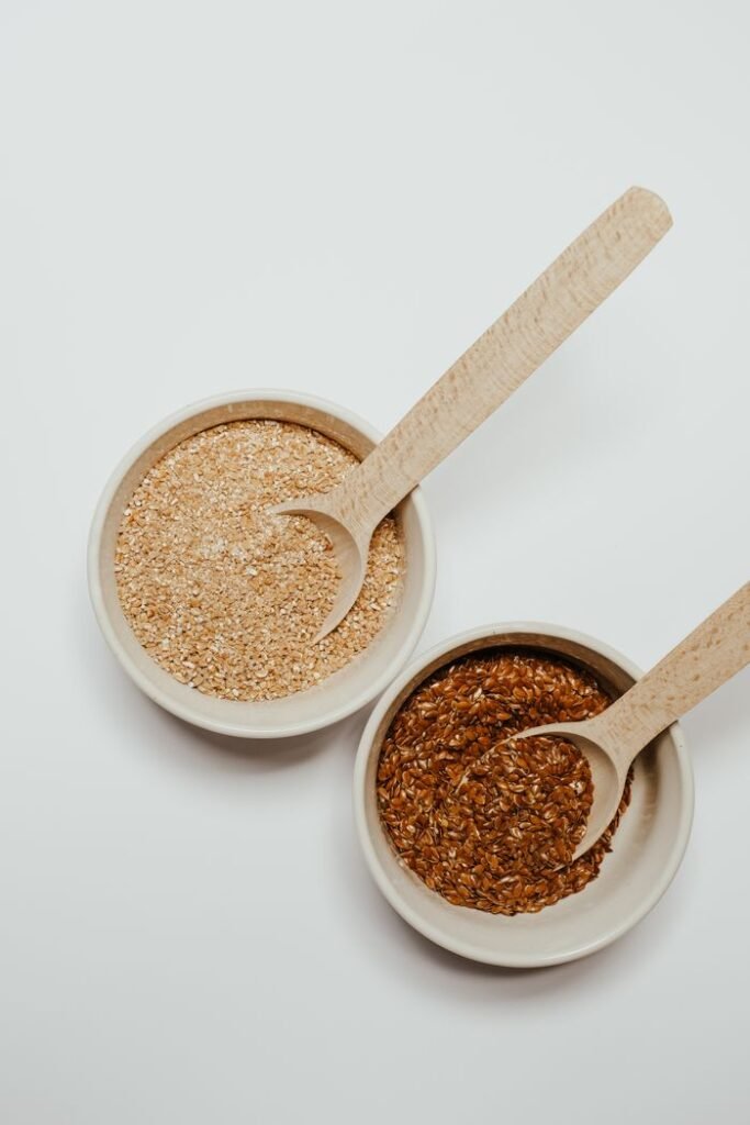 pexels photo 7420736 7420736 Elegant flat lay of flax and oat seeds in ceramic bowls with wooden spoons on a white background.